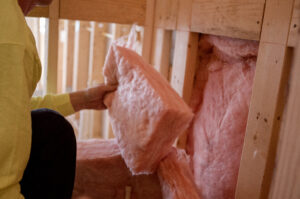 A technician adding fiberglass batt insulation to a wall
